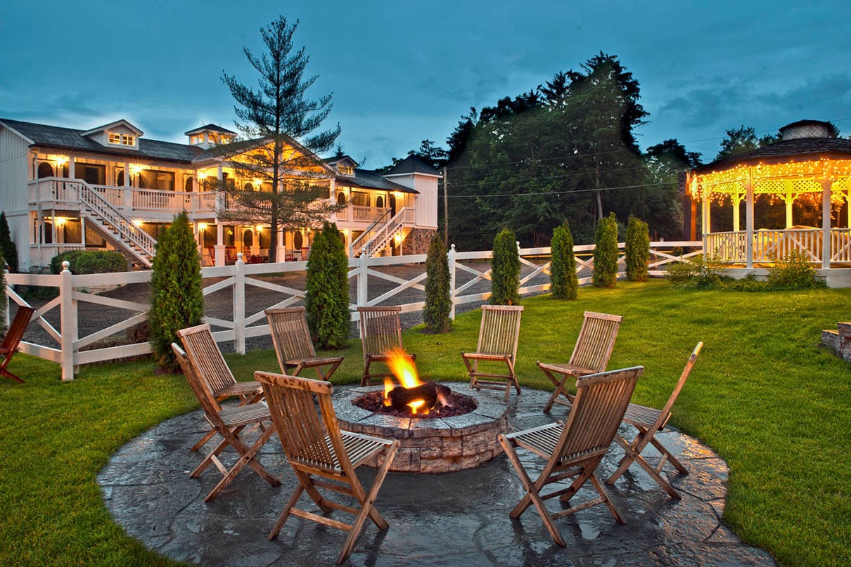 A fire pit surrounded by chairs with a gazebo and hotel in background